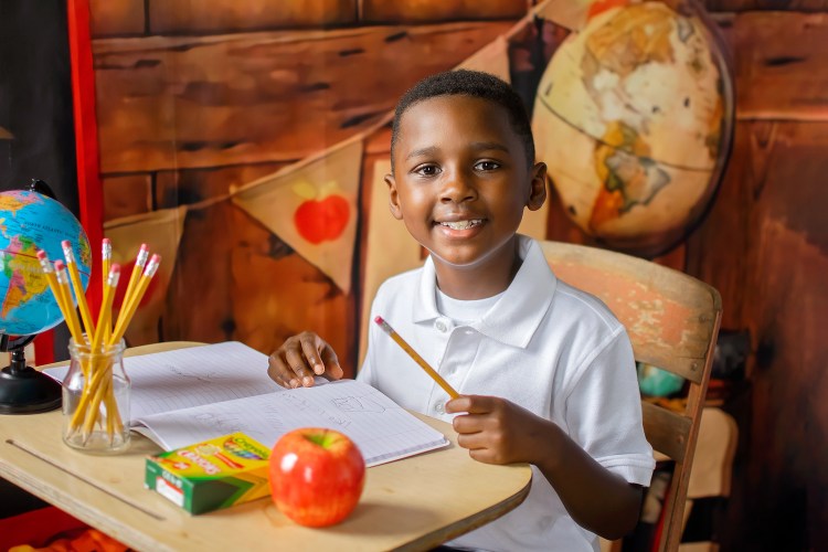 Smiling preschool boy holding an apple during boutique school picture day with Phoenix Productions ATL in Atlanta, Georgia.